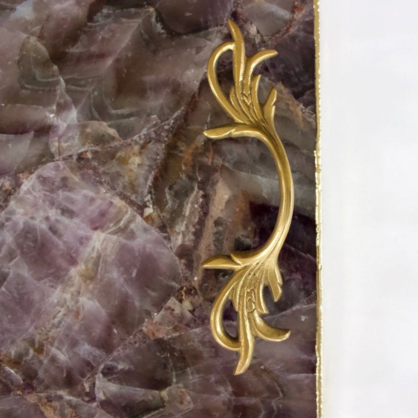 Decorative gold metal drawer handle on purple marble surface from The Tangerine Store