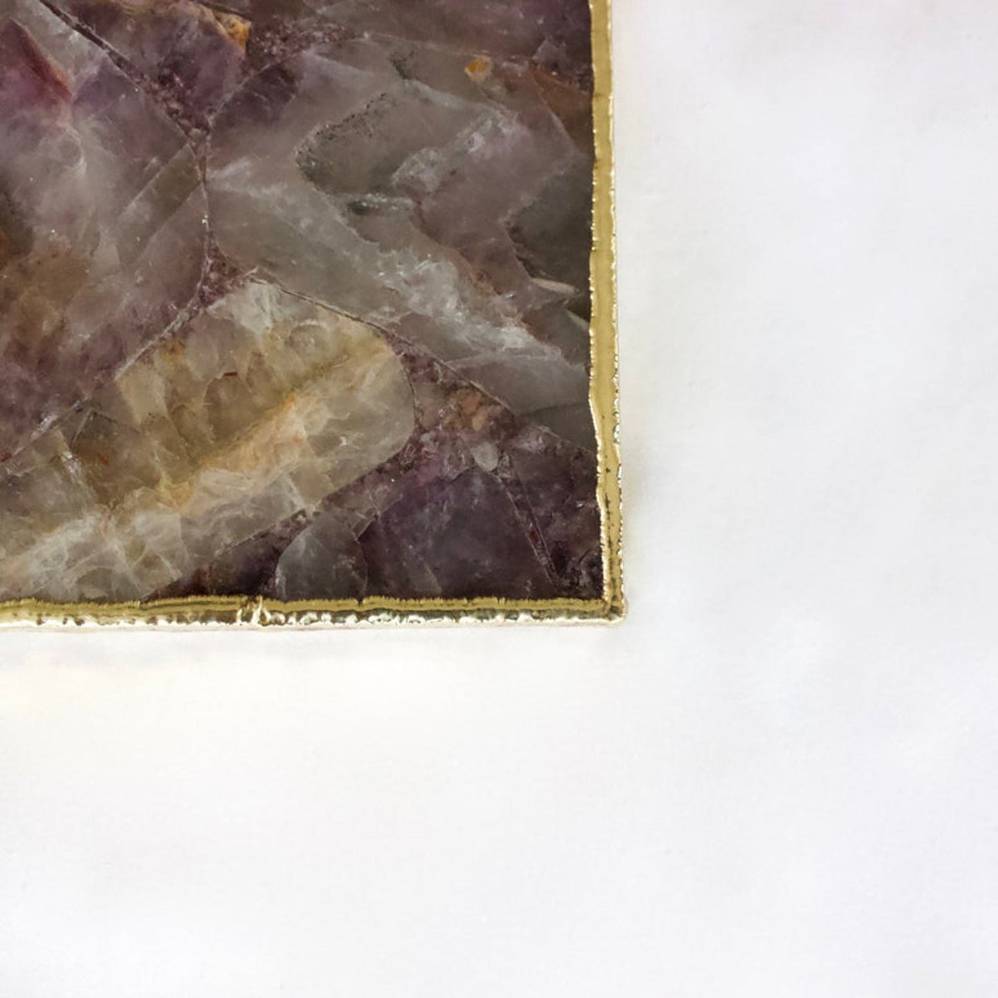 Close-up of a polished purple and beige stone slab with gold-edged frame on white background