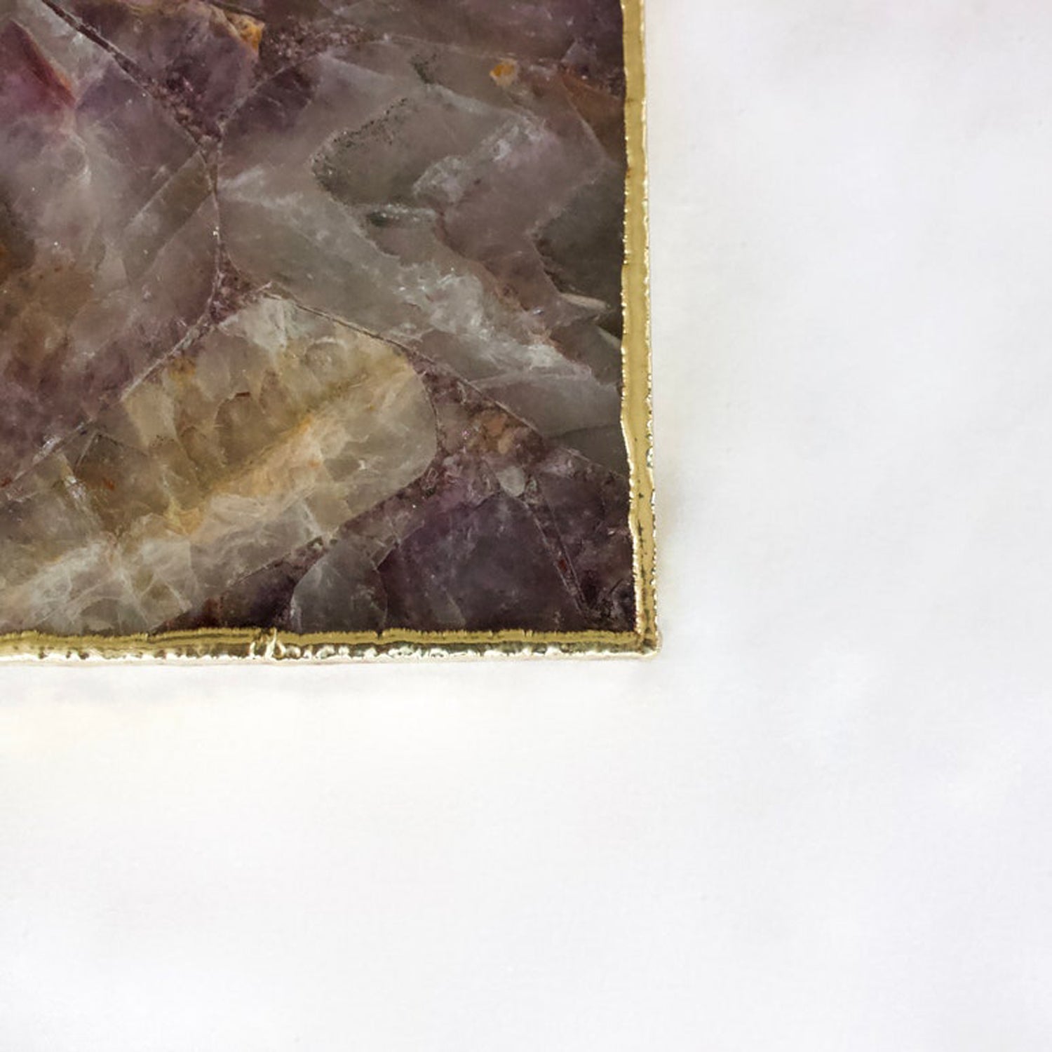 Close-up of a polished purple and beige stone slab with gold-edged frame on white background