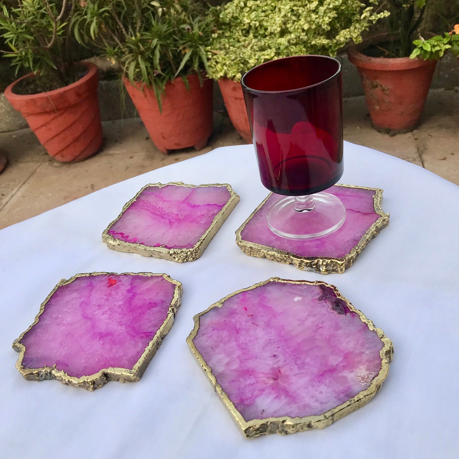 Large pink agate drink coasters with gold edges displayed on white table with red glass