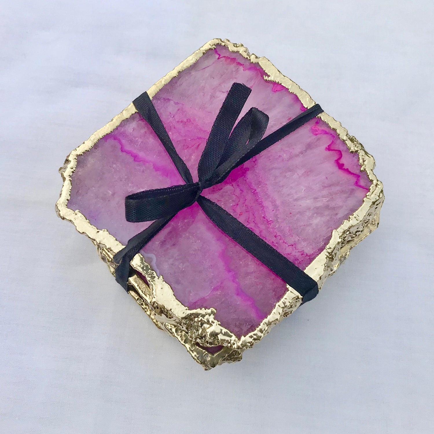 Set of large pink agate drink coasters with gold edges tied with a black ribbon